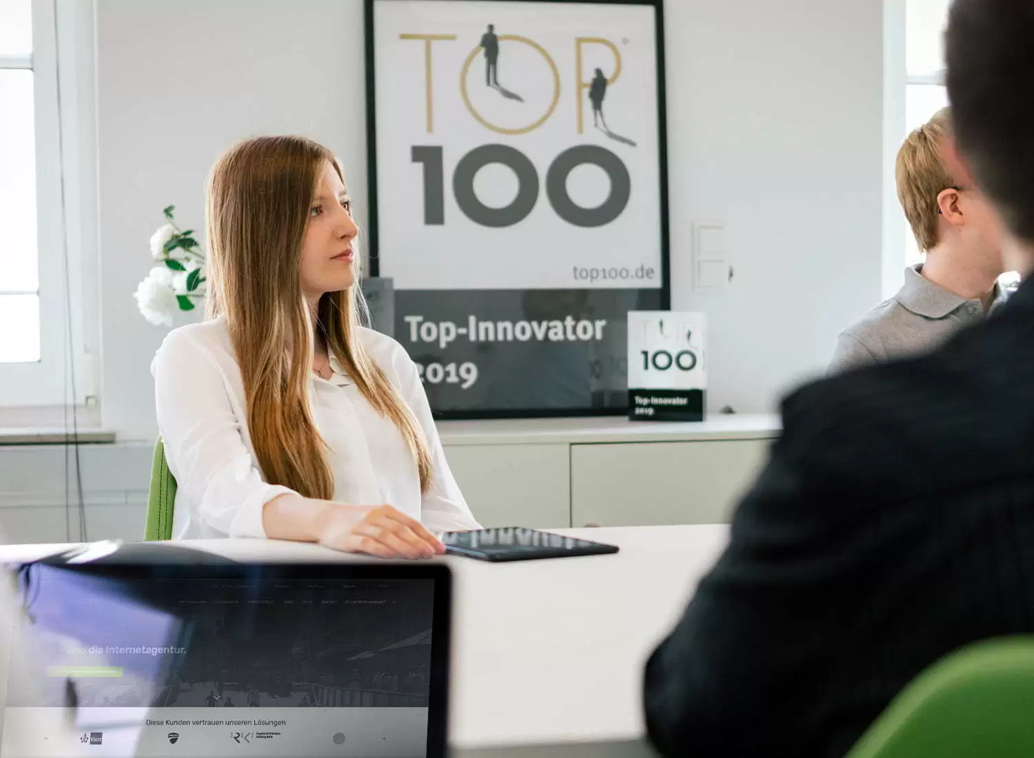 Online-Marketing-Beratung: Experten im Gespräch Mitarbeiterin in einem Meeting zum Thema Online-Marketing-Beratung, im Hintergrund ein Top-Innovator-Award