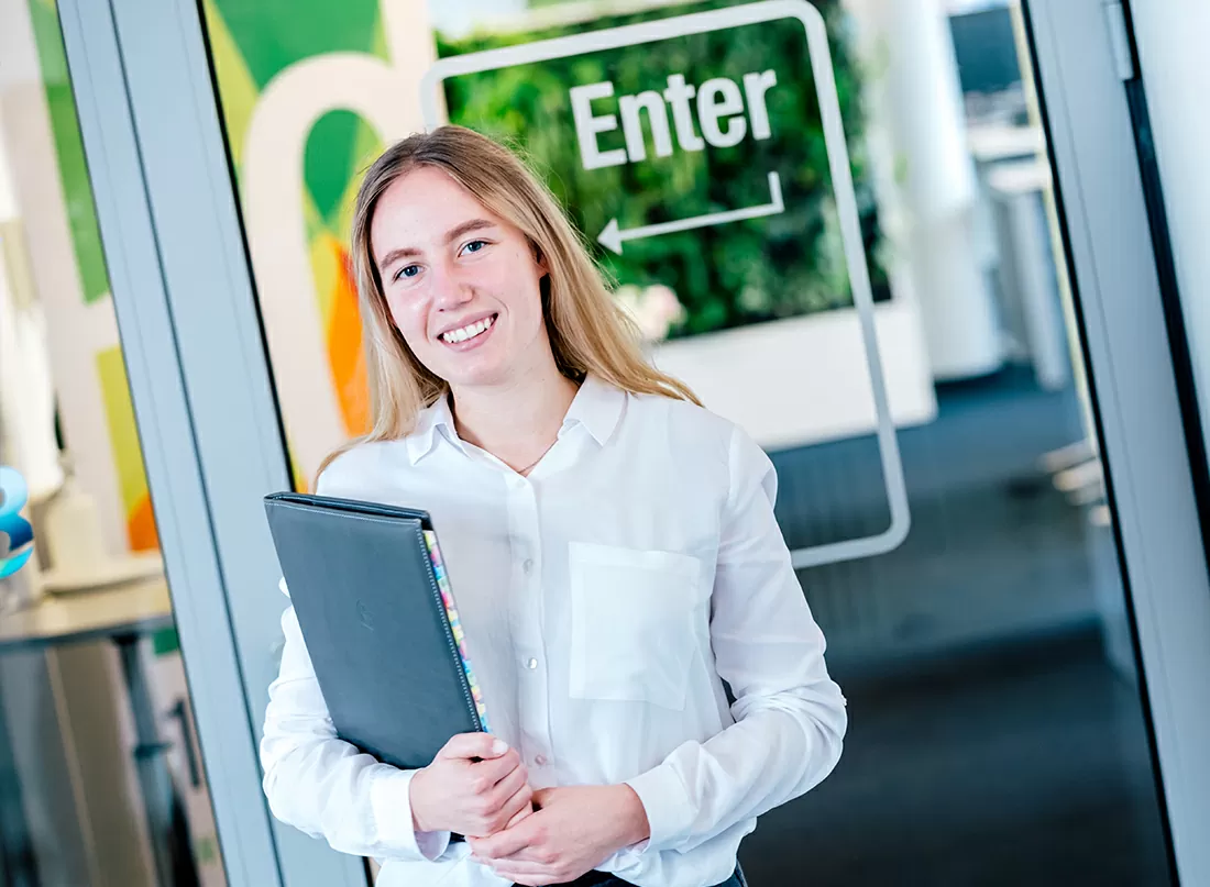 Mitarbeiterin steht mit einem Ordner vor dem Besprechungsraum