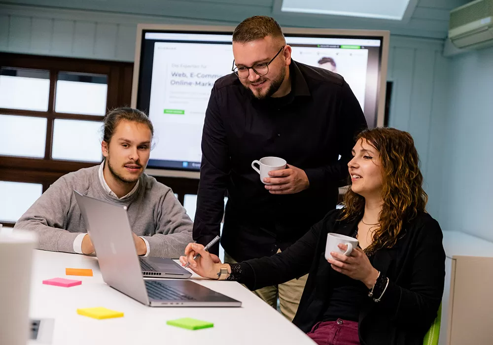Online-Marketing-Agentur in Mannheim Drei Personen vor einem Laptop in einem Büroraum.