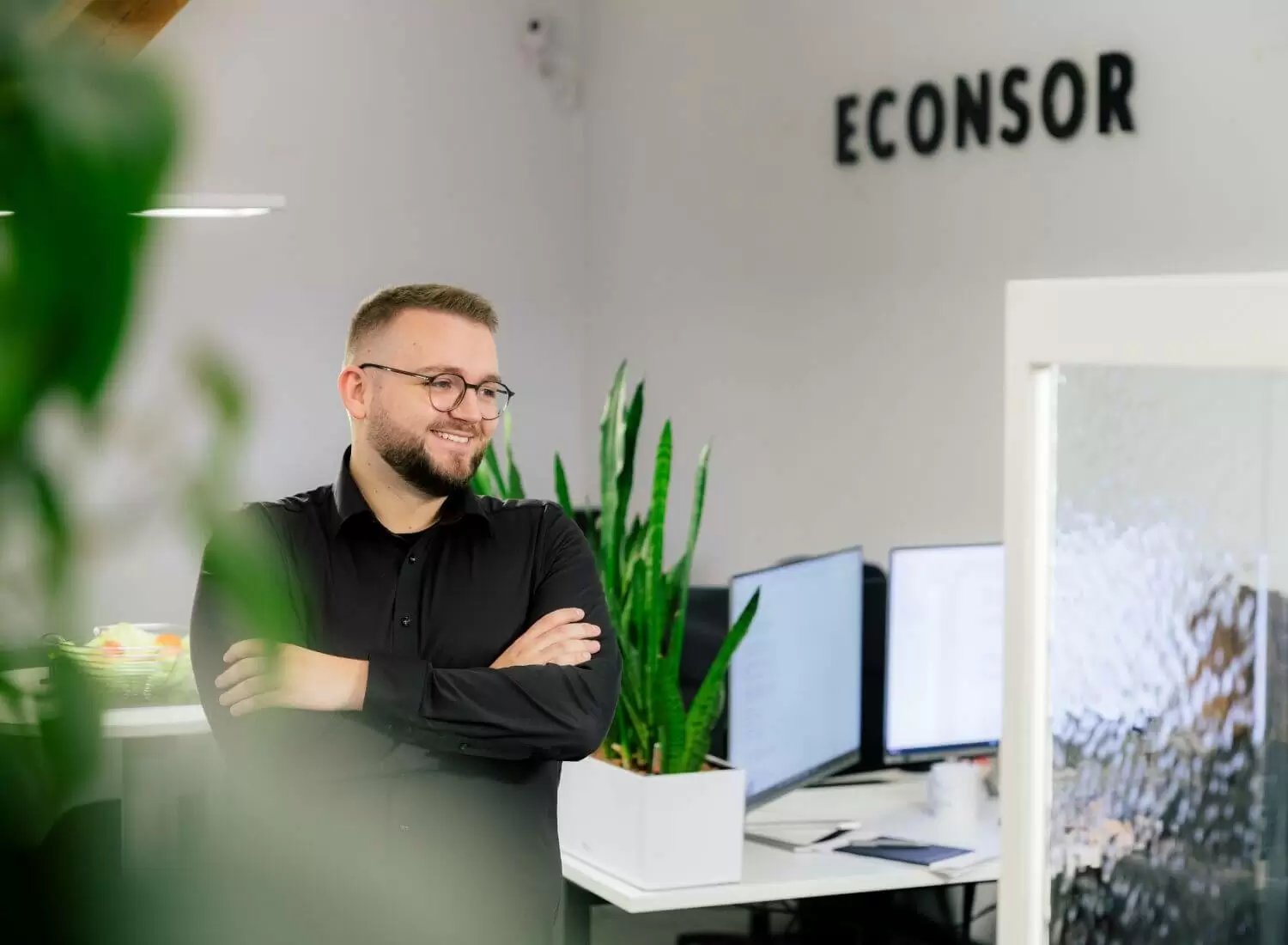Internetagentur in Mannheim Junger mann steht in einem Büro. Im Hintergrund sieht man Arbeitsplätze.