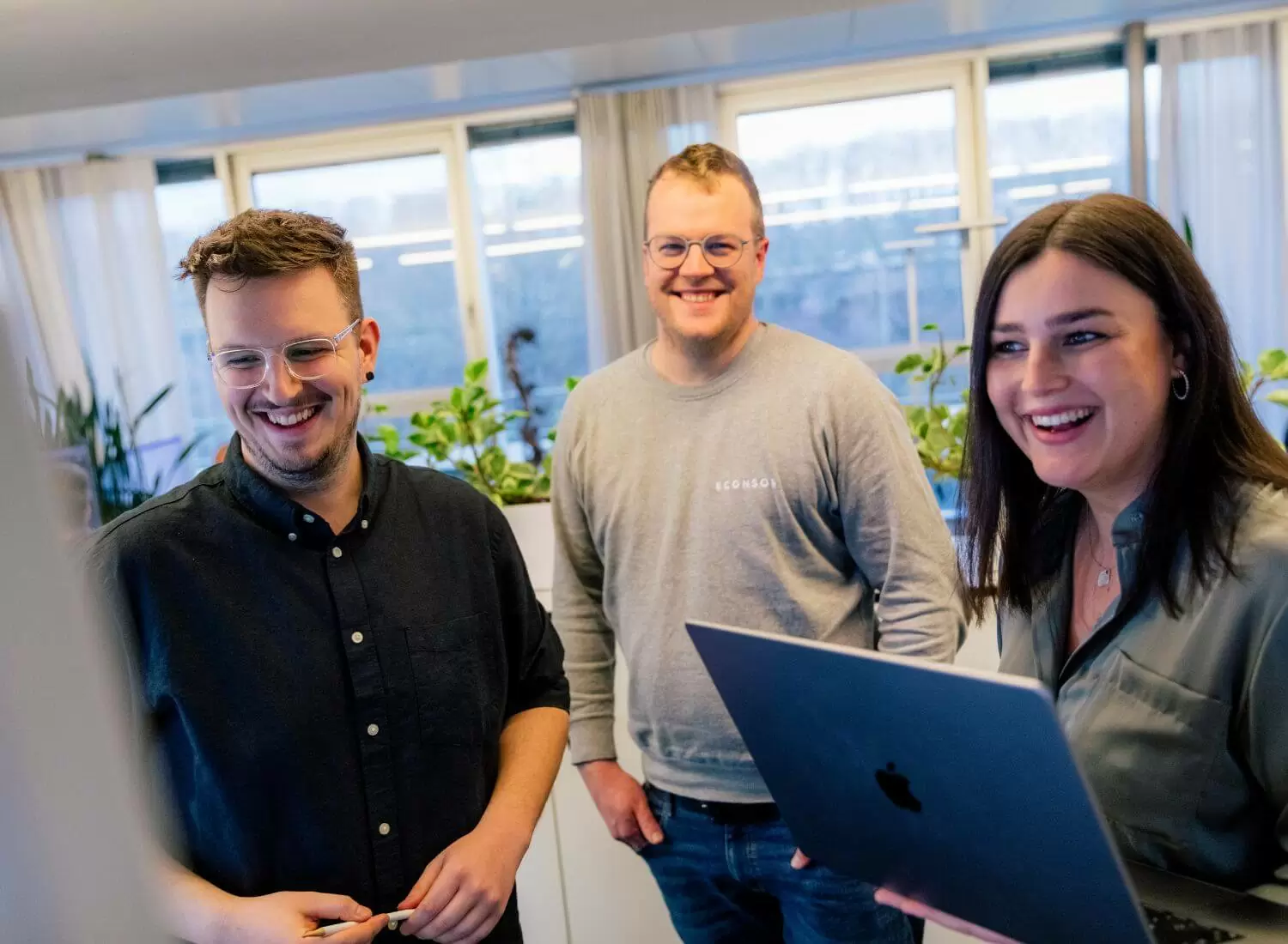 Magento-Spezialisten in Mannheim Drei junge Menschen stehen lächelnd vor einem Smartboard