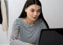 Frau sitzt am PC umgeben von Kartons und Kleidung